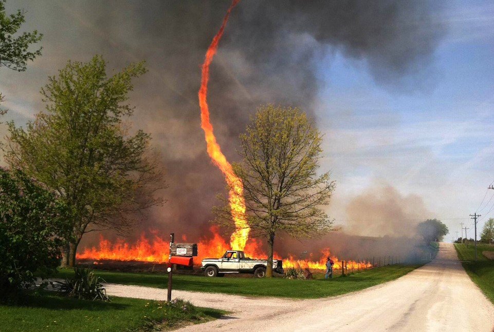 A massive firenado swirls above the Deer Creek Fire near La Sal, Utah, with intense orange flames and rotating wind columns.