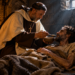 Saint John of the Cross caring for a prisoner in a dark stone cell, illustrating his years of suffering and faith